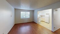 This single-floor unit offers a straightforward and functional layout designed for comfortable everyday living. The entry opens into a bright living area finished with warm hardwood-style laminate flooring that extends throughout the main living spaces. A large window allows natural light to fill the room while offering a view of surrounding greenery, creating an inviting and airy atmosphere. The textured popcorn ceiling is consistent throughout, adding a classic touch to the interior.

The kitchen is accessible directly from the living area through an open pass-through design. It features white cabinetry with ample upper and lower storage, light-toned countertops, a double-basin sink positioned beneath a window, and white appliances including a gas range and refrigerator. The kitchen floor is finished with vinyl tile, providing a practical and easy-to-maintain surface.

The bedroom is a well-sized, quiet retreat with plush carpeting underfoot and two windows that bring in natural light from multiple angles. A ceiling fan with an integrated light fixture adds both comfort and functionality to the space.

The bathroom is neatly appointed with a white vanity, a built-in medicine cabinet mirror, tile-surround tub and shower combination, and light tile flooring — all presented in a clean, all-white finish that keeps the space feeling fresh and bright.