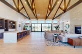 Located at 22624 E Radcliff Cir in Aurora, CO, this thoughtfully designed single-floor community space blends rustic character with modern sophistication. The architectural centerpiece is the dramatic vaulted ceiling adorned with exposed dark wood trusses set against natural wood planking, creating an atmosphere that is both grand and warm. Light-toned hardwood flooring runs throughout, unifying the open layout seamlessly.

The main living area is generously proportioned, anchored by a floor-to-ceiling stone fireplace flanked by illuminated built-in bookshelves. Oversized sliding glass doors open to expansive views of an outdoor pool and patio, flooding the space with natural light. A long bar counter with seating and integrated shelving serves as both a social hub and functional gathering point beneath the soaring roofline.

A second living area offers a more intimate setting, featuring large windows with neighborhood views, comfortable lounge seating, and a sculptural pendant light that adds artistic flair. The combined dining and living room is bright and airy, highlighted by tall windows, a striking floral chandelier, and a built-in display niche. Throughout the space, contemporary furnishings and carefully considered lighting create a cohesive, inviting ambiance ideal for community gathering and relaxation.