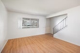 Located at 21418 Bloomfield Ave in Lakewood, CA, this two-story, 2-bedroom, 2-bathroom home offers a well-organized layout with equal square footage distributed across both floors. The main level welcomes you through a formal entrance that opens into a bright, open living room featuring warm wood-look flooring and a large window that draws in natural light with views of the greenery outside. A staircase with a sleek black metal railing connects the two floors. The combined dining and kitchen area is functional and well-appointed, featuring white cabinetry, granite-style countertops, black appliances including a gas range and dishwasher, and a sliding glass door leading directly to a private outdoor patio — ideal for casual outdoor relaxation. A full bathroom with a tub and vanity with stone-topped counters completes the lower level. Upstairs, both bedrooms are carpeted for comfort, with the spacious primary bedroom offering ample natural light. The upper-level bathroom features a walk-in style shower with glass enclosure, a matching vanity, and wood-look flooring. Multiple closets throughout the home provide generous storage. The overall aesthetic is clean, neutral, and move-in ready.