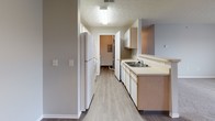 This single-floor residence on Claudia Drive in London, Ohio offers a straightforward, functional layout designed for comfortable everyday living. Neutral gray walls and textured ceilings are consistent throughout, creating a cohesive and clean aesthetic across all rooms.

The living area features plush wall-to-wall carpeting and flows openly toward a dining area distinguished by wood-look vinyl flooring and a pendant light fixture overhead. A wall-mounted thermostat and multiple electrical outlets are conveniently positioned throughout the living space.

The galley-style kitchen runs along a narrow corridor and is equipped with light wood cabinetry, a double-basin sink, a white refrigerator, a dishwasher, and laminate countertops. Wood-look vinyl flooring continues through the kitchen, and a utility area with additional mechanical access is visible at the far end.

The bedrooms are carpeted and generously proportioned, each receiving natural light through windows. Closet space is provided in the bedrooms, with at least one featuring a reach-in closet with a rod and shelf system.

Two full bathrooms serve the unit, each finished with wood-look vinyl flooring, a vanity with under-sink storage, a toilet, and a tub-shower combination. The overall design prioritizes practicality, with a clean, move-in-ready condition throughout.