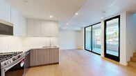 Located in the heart of West Hollywood, this contemporary two-story residence at 1257 N Detroit St. offers a thoughtfully designed layout spread across two levels. The main floor hosts an open-concept living room and kitchen, finished with wide-plank light oak hardwood flooring and recessed lighting throughout. Floor-to-ceiling sliding glass doors flood the living area with natural light and open directly onto a private outdoor patio, creating a seamless indoor-outdoor flow. The kitchen is outfitted with stainless steel appliances including a gas range, built-in microwave, and dishwasher, complemented by quartz countertops, a marble-inspired backsplash, a deep stainless sink, and a combination of white upper cabinetry and warm wood-toned lower cabinets. A sculptural staircase with sleek metal railings leads to the upper level, where the bedroom features tall black-framed windows that frame outdoor views and fill the room with abundant natural light, along with a double-door closet with refined wood-grain finishes. The full bathroom presents a spa-like atmosphere with a soaking tub and overhead rain shower, warm stone-toned wall panels, a floating wood vanity, and white quartz countertop. Clean lines and a neutral palette define the overall aesthetic of this modern West Hollywood residence.