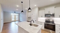 Located at 7100 Summerside Dr in Whitsett, NC, this well-appointed 2-bedroom, 1-bathroom single-story home offers a thoughtfully designed open-concept layout. The kitchen and living room flow seamlessly together, anchored by a central island topped with striking granite countertops and fitted with a matte black undermount sink. Crisp white shaker cabinets, stainless steel appliances — including a refrigerator, microwave, and electric range — and pendant lighting with matching black fixtures lend the kitchen a clean, modern aesthetic. A built-in desk nook adjacent to the kitchen adds a practical touch. Light hardwood flooring runs throughout the main living areas, complemented by recessed lighting and a ceiling fan. French doors invite natural light into the living space. Both bedrooms feature plush carpeting, ceiling fans, and windows with views of the surrounding neighborhood. The bathroom maintains the home's cohesive design with granite counters, white cabinetry with black hardware, a glass-enclosed shower, and hardwood-style flooring. A dedicated laundry room houses a full-sized washer and dryer with overhead wire shelving for additional storage. The home's neutral palette and modern finishes create a bright, inviting atmosphere throughout.