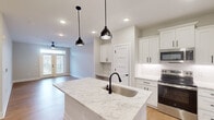 Located at 7100 Summerside Dr in Whitsett, NC, this well-appointed 2-bedroom, 1-bathroom single-story home offers a thoughtfully designed open-concept layout. The kitchen and living room flow seamlessly together, anchored by a central island topped with striking granite countertops and fitted with a matte black undermount sink. Crisp white shaker cabinets, stainless steel appliances — including a refrigerator, microwave, and electric range — and pendant lighting with matching black fixtures lend the kitchen a clean, modern aesthetic. A built-in desk nook adjacent to the kitchen adds a practical touch. Light hardwood flooring runs throughout the main living areas, complemented by recessed lighting and a ceiling fan. French doors invite natural light into the living space. Both bedrooms feature plush carpeting, ceiling fans, and windows with views of the surrounding neighborhood. The bathroom maintains the home's cohesive design with granite counters, white cabinetry with black hardware, a glass-enclosed shower, and hardwood-style flooring. A dedicated laundry room houses a full-sized washer and dryer with overhead wire shelving for additional storage. The home's neutral palette and modern finishes create a bright, inviting atmosphere throughout.
