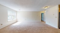 Located at 401 Talcottville Rd in Vernon Rockville, Connecticut, this single-floor residence offers a clean, neutral aesthetic throughout. The spacious main living area is covered in plush beige carpeting and bathed in natural light from large windows fitted with blinds, creating a bright and welcoming atmosphere. Textured ceilings and crisp white trim complement the warm, cream-toned walls found throughout the home.

The galley-style kitchen is well-appointed with warm maple cabinetry, dark granite countertops, and a stainless steel gas range, all illuminated by a window that brings in natural light. Adjacent to the kitchen, the layout flows seamlessly into the open living spaces.

The bedrooms are generously sized, each featuring soft carpeting, large windows with views of surrounding greenery, and ample closet space. One bedroom notably includes a walk-in closet alongside an additional double-door closet, providing excellent storage capacity.

The bathroom is finished with warm-toned stone tile flooring, a white vanity with a dark countertop, and a window that ensures natural ventilation and light. A staircase with a classic wooden banister is also visible, adding a traditional architectural detail to the overall design. This residence combines functional layout with comfortable, understated finishes throughout.