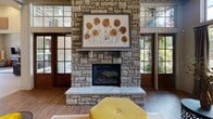 Located at 6837 N Trenholm Rd in Arcadia Lakes, SC, this single-floor community space combines elegant design with welcoming functionality. The interior is defined by dramatically high ceilings accented with board-and-batten paneling painted in a cool gray tone, lending a refined, contemporary farmhouse character throughout.

The expansive main lounge area serves as the heart of the space, anchored by a striking floor-to-ceiling stone fireplace flanked by large glass-paned doors that invite abundant natural light and outdoor views. Rich hardwood flooring flows seamlessly throughout, complementing the warm, layered furnishings that include plush leather sofas, patterned accent chairs, and decorative side tables.

Multiple seating arrangements create distinct gathering zones — one centered around a media console with open metal shelving, and another oriented toward the fireplace — offering both casual and social settings. A woven rattan mirror and curated décor accents add texture and visual interest to the walls.

The kitchen area features dark wood cabinetry, mosaic tile backsplash, stainless steel appliances, and a generously sized granite-topped bar with seating — ideal for entertaining. A globe chandelier overhead adds a stylish focal point. Large windows throughout the space frame views of the surrounding landscape, enhancing the bright, airy ambiance of this thoughtfully designed gathering venue.