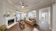 This thoughtfully designed 2-bedroom, 2-bathroom single-floor residence offers a comfortable and functional layout across a well-proportioned footprint. The living room serves as the centerpiece of the home, boasting a striking tray ceiling with crown molding, a ceiling fan, a classic white fireplace, and rich hardwood flooring. Large windows and a glass door flood the space with natural light while offering outdoor views. An arched opening connects the living area to the dining room, which features elegant wainscoting and crown molding details.

The kitchen is outfitted with white cabinetry, stainless steel appliances including a range and refrigerator, a center island with sink, and light tile flooring — offering ample counter and storage space. The adjoining dining area provides a defined space for meals.

The primary bedroom is a generous retreat with large windows on two walls, plush carpet, and a ceiling fan, complemented by a spacious walk-in closet with built-in wire shelving. The second bedroom also features carpet, a ceiling fan, and a large window with outdoor views. Each bathroom is finished with tile flooring, white cabinetry, and clean, neutral tones — one featuring an extended vanity and a walk-in shower.