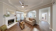 This thoughtfully designed 2-bedroom, 2-bathroom single-floor residence offers a comfortable and functional layout across a well-proportioned footprint. The living room serves as the centerpiece of the home, boasting a striking tray ceiling with crown molding, a ceiling fan, a classic white fireplace, and rich hardwood flooring. Large windows and a glass door flood the space with natural light while offering outdoor views. An arched opening connects the living area to the dining room, which features elegant wainscoting and crown molding details.

The kitchen is outfitted with white cabinetry, stainless steel appliances including a range and refrigerator, a center island with sink, and light tile flooring — offering ample counter and storage space. The adjoining dining area provides a defined space for meals.

The primary bedroom is a generous retreat with large windows on two walls, plush carpet, and a ceiling fan, complemented by a spacious walk-in closet with built-in wire shelving. The second bedroom also features carpet, a ceiling fan, and a large window with outdoor views. Each bathroom is finished with tile flooring, white cabinetry, and clean, neutral tones — one featuring an extended vanity and a walk-in shower.
