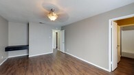 This two-floor space showcases a cohesive design centered around dark hardwood-style flooring and neutral gray walls that carry consistently throughout every room, creating a unified and modern aesthetic. The main level features an open living area anchored by a staircase leading to the upper floor, with two doors providing access to additional rooms or storage. Natural light filters in through blinded windows, contributing to a calm, well-lit atmosphere.

The galley-style kitchen is outfitted with dark cabinetry, granite-style countertops, black appliances including a refrigerator and cooktop, and a sink — offering a functional and visually striking workspace. Adjacent dining and living areas are illuminated by pendant light fixtures with a classic bowl design, adding warmth to the neutral palette.

The bathrooms feature granite-style countertops with vessel sinks, dark vanity cabinetry, and a tub-shower combination with white tile surround. A window in the bathroom provides natural ventilation and light. The upper level contains additional rooms, each fitted with ceiling-mounted light fixtures and windows allowing natural light to enter. Throughout the space, white trim and baseboards provide clean contrast against the gray walls and dark flooring.