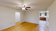 This well-organized single-floor unit offers a thoughtful layout comprising a living room, bedroom, kitchen, bathroom, and hallway. Warm hardwood flooring flows consistently through the living areas and bedroom, lending a cohesive and inviting feel throughout the space. Each room is equipped with a ceiling fan fitted with a light kit, providing both air circulation and ambient lighting.

The living room receives ample natural light through a large multi-pane window and a glass-paneled entry door that overlooks the outdoors. A wall-mounted HVAC unit provides supplemental climate control. The bedroom features two closets — one walk-in style and one with louvered bi-fold doors — alongside a window with outdoor views, offering practical storage and natural light.

The kitchen is outfitted with rich medium-toned wood cabinetry, light granite-style countertops, and white appliances including a gas range, built-in microwave, and refrigerator. Light ceramic tile flooring and a window above the sink bring brightness to the space. A secondary exterior door in the kitchen provides additional access.

The bathroom is finished with large-format neutral wall and floor tiles, a soaking tub with a shower and curtain rod, a window for natural ventilation, and a white vanity with overhead cabinet storage, creating a clean, functional environment.