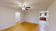 This well-organized single-floor unit offers a thoughtful layout comprising a living room, bedroom, kitchen, bathroom, and hallway. Warm hardwood flooring flows consistently through the living areas and bedroom, lending a cohesive and inviting feel throughout the space. Each room is equipped with a ceiling fan fitted with a light kit, providing both air circulation and ambient lighting.

The living room receives ample natural light through a large multi-pane window and a glass-paneled entry door that overlooks the outdoors. A wall-mounted HVAC unit provides supplemental climate control. The bedroom features two closets — one walk-in style and one with louvered bi-fold doors — alongside a window with outdoor views, offering practical storage and natural light.

The kitchen is outfitted with rich medium-toned wood cabinetry, light granite-style countertops, and white appliances including a gas range, built-in microwave, and refrigerator. Light ceramic tile flooring and a window above the sink bring brightness to the space. A secondary exterior door in the kitchen provides additional access.

The bathroom is finished with large-format neutral wall and floor tiles, a soaking tub with a shower and curtain rod, a window for natural ventilation, and a white vanity with overhead cabinet storage, creating a clean, functional environment.