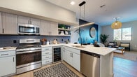 Located in the heart of Scottsdale on E Main St, this thoughtfully designed one-bedroom, one-bathroom residence offers a well-appointed open-concept layout with modern finishes and a warm contemporary aesthetic. The kitchen is a standout feature, showcasing stainless steel appliances including a gas range, built-in microwave, and dishwasher, complemented by crisp white quartz countertops, dual-tone cabinetry with light wood uppers and soft grey lowers, a subway tile backsplash, open shelving, and a built-in wine cooler. A sleek linear pendant light anchors the kitchen peninsula, which flows seamlessly into the dining and living areas. The living room is bright and airy, with natural light streaming through multiple windows offering outdoor views of the surrounding Scottsdale landscape. A bold teal accent wall adds a vibrant design element that carries through the main living spaces. The dining nook is cozy and intimate, bordered by a rich charcoal accent wall. The bedroom is a serene retreat featuring a dramatic striped wood accent wall, a large sliding glass door opening to a private balcony with city views, and direct access to a walk-in closet. The bathroom is clean and modern, featuring warm wood cabinetry, a wide vanity with a large mirror, and light hardwood-style flooring that extends throughout the residence.