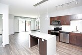 This contemporary single-floor residence offers a thoughtfully designed layout that balances comfort and modern style. The open-concept living and kitchen area serves as the heart of the unit, featuring durable wood-look plank flooring and large sliding glass doors that invite abundant natural light and provide direct access to an outdoor balcony with urban views. The kitchen is outfitted with rich, dark espresso cabinetry, granite-look countertops, a subway tile backsplash, a central island with pendant lighting, and a full suite of stainless steel appliances including a range, microwave, dishwasher, and refrigerator. The bedrooms are carpeted for comfort and each features oversized black-framed windows that frame greenery and city views while filling the rooms with natural light. The full bathroom includes a tub-shower combination, a dark-cabinetry vanity with a granite-look countertop, a large mirror, and wood-look flooring. A second half or three-quarter bathroom echoes the same finishes, offering an elongated layout with a matching vanity and toilet. Throughout the unit, a neutral color palette, clean lines, and consistent modern finishes create a cohesive and inviting atmosphere.