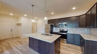 Located at 205 Ellis Park in Lexington, Kentucky, this single-floor home offers a thoughtfully designed open-concept layout that seamlessly connects the kitchen and living areas. The kitchen serves as the centerpiece of the space, showcasing a large island with a granite countertop, double sink, and pendant lighting overhead. Dark espresso-toned cabinetry extends to the ceiling, complemented by a subway tile backsplash and a full suite of stainless steel appliances, including a refrigerator, range, microwave, and dishwasher. Recessed lighting and crown molding add refined finishing touches throughout. The living area flows naturally from the kitchen and features wood-look plank flooring, a ceiling fan, and access to a front entryway. Bedrooms are well-proportioned with natural light from window treatments and include walk-in closet storage with built-in shelving. The bathrooms are finished with the same dark cabinetry and granite vanity surfaces, with one bathroom offering a glass-enclosed walk-in shower and another featuring a full soaking tub. Light tile flooring completes the bathrooms' clean, contemporary aesthetic. Overall, the home presents a cohesive, modern design with quality finishes throughout.