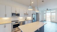 Located at 1000 Lakeside Terrace Ct in Wake Forest, NC, this well-appointed single-floor residence offers a thoughtfully designed layout across a comfortable footprint. The open-concept kitchen serves as a centerpiece of the home, showcasing white shaker-style cabinetry with gold hardware, a white subway tile backsplash, light quartz countertops, and a bold navy-accented island with a clean quartz surface. Stainless steel appliances — including a French door refrigerator, range, microwave, and dishwasher — complete the space, while pendant lighting with gold accents adds a refined touch. Wood-look flooring extends through the main living and kitchen areas, lending warmth and continuity. The living space opens to a private balcony through floor-to-ceiling glass doors, allowing generous natural light and outdoor views of the surrounding neighborhood. Ceiling fans are installed in key rooms for added comfort. The bedrooms feature plush carpeting and ample natural light from well-placed windows. A spacious walk-in closet with wire shelving provides generous storage. Both bathrooms are finished with white vanity cabinetry, gold and matte black hardware, large framed mirrors, and stylish multi-bulb light fixtures atop wood-look tile flooring. An in-unit laundry area adds everyday convenience to this move-in-ready home.
