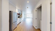 Located at 9675 Avenue Papineau in Montréal, this modern one-bedroom, one-bathroom unit offers a thoughtfully designed open-concept layout finished with clean, contemporary details throughout. Light wood laminate flooring runs continuously across the entire space, complementing the crisp white walls and recessed lighting that keep the interior feeling bright and airy.

The kitchen and living area flow seamlessly together in a long, open format. The kitchen is equipped with stainless steel appliances — including a full-size refrigerator, range, and over-the-range microwave — set against sleek white cabinetry and a warm wood-toned countertop. A pendant light anchors the transition toward the living area, which is bathed in natural light from oversized floor-to-ceiling windows and a glass door that open to views of the surrounding neighbourhood.

The spacious bedroom features its own window for natural light, a dedicated closet, and easy access to in-unit stacked laundry. The full bathroom is finished to a high standard, with large-format beige tiles, a glass-enclosed walk-in shower, a wall-mounted wood vanity with a vessel sink, and a wide mirror. A dedicated closet provides additional storage. The overall ambiance is modern, clean, and functional — well-suited for comfortable urban living in Montréal.