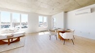 Located at 2255 Boul Daniel Johnson in Laval, QC, this thoughtfully designed one-bedroom, one-bathroom unit offers a contemporary urban living experience with generous overall floor area. The space is defined by its striking exposed concrete ceilings, which lend an industrial-modern character throughout, complemented by light hardwood flooring that adds warmth and continuity across every room.

The open-concept living and dining area is a highlight of the unit, bathed in natural light through large windows that frame views of the surrounding cityscape. The spacious layout comfortably accommodates both a lounge and dining area, with a wall-mounted mini-split system ensuring year-round comfort.

The kitchen features sleek flat-panel cabinetry in white and light wood tones, white quartz countertops, stainless steel appliances including a refrigerator and range, and a functional island with an integrated sink — ideal for both cooking and casual dining.

The bedroom offers a tranquil retreat, benefiting from natural light through a generously sized window with outdoor views, an exposed concrete ceiling, and a built-in closet. The bathroom is finished with large-format beige tiles, a wood-toned vanity, and a full soaking tub with tiled surround. A bright entry corridor with additional storage completes this well-appointed urban residence.