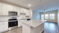 This single-floor residence in South Fulton, Georgia, presents a clean, contemporary design throughout its well-appointed layout. The kitchen serves as a central highlight, outfitted with crisp white shaker cabinetry, granite countertops, and a full suite of stainless steel appliances including a range, microwave, dishwasher, and refrigerator. A generously sized island with matching granite provides additional prep and seating space, while a subway tile backsplash adds a polished finishing touch. Wood-style flooring runs through the main living areas, complementing the neutral color palette.

The living area is bright and open, with large windows that invite natural light and provide outdoor views, accompanied by a ceiling fan overhead. A door leads directly to a private outdoor space. The private quarters are carpeted for comfort and connected by a hallway that includes built-in shelving for additional storage. The bathroom features a dual-sink vanity with granite countertops, white cabinetry, and wood-style flooring. Closet space is well-considered, with a walk-in closet and additional shelved storage. A dedicated laundry room houses a full-size washer and dryer, rounding out the functional amenities of this thoughtfully designed space.