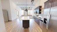 Located in the heart of downtown Johnson City, Tennessee, this 2-bedroom, 2-bathroom urban loft blends industrial character with modern finishes across a single, well-appointed floor. The open-concept kitchen and living area anchors the space, showcasing soaring ceilings with exposed ductwork and pendant lighting that lend an authentic loft aesthetic. The kitchen is thoughtfully equipped with rich dark cabinetry, stainless steel appliances, a tile backsplash, quartz countertops, open floating shelves, and a substantial center island—ideal for cooking and entertaining. Light hardwood flooring runs throughout the main living and kitchen areas, creating warmth against the industrial backdrop. Both bedrooms are generously sized with plush carpeting, tall ceilings, and large windows framed in rustic wood trim that fill the rooms with natural light and offer views of the surrounding cityscape. Ceiling fans add comfort to each bedroom. The two bathrooms are finished with dark wood vanities, quartz countertops, and chrome fixtures; one features a tub-shower combo. Two closets provide ample storage. The overall ambiance strikes a refined balance between contemporary urban living and industrial charm, making this a distinctive offering in downtown Johnson City.