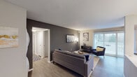 This single-floor residence offers a thoughtfully designed layout with a cohesive modern aesthetic. The living room serves as the central gathering space, featuring warm wood-look flooring, a bold dark gray accent wall, and a large sliding glass door that invites natural light and provides outdoor views. The open arrangement comfortably accommodates a seating area and flows naturally into the rest of the unit.

The kitchen is well-equipped with stainless steel appliances, including a range, microwave, and refrigerator. White shaker-style cabinetry, a mosaic tile backsplash, and a dark island with a light countertop provide both functionality and visual contrast. A tall pantry cabinet adds generous storage.

Two bedrooms offer comfortable retreats, each with plush carpeting, vertical blinds on windows that allow natural light, and dedicated closet space. One bedroom includes a walk-in closet, while both rooms provide ample room for furnishings.

The two bathrooms are finished with dark vanity cabinetry and granite-style countertops. One bathroom features a tub-shower combination with white tile surround, while the other offers a glass-enclosed shower with wood-look flooring, rounding out this well-balanced residence.