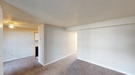 This single-floor residential unit offers a practical and straightforward layout designed for comfortable everyday living. The spacious living area features neutral-toned carpet, clean white walls, and a textured ceiling, creating a bright and open atmosphere. A large window allows natural light to fill the space, while a door provides direct exterior access. The living area connects seamlessly to the kitchen, which is equipped with light wood cabinetry, a double-basin sink, tile flooring, and black appliances including a refrigerator, range, and dishwasher, offering ample functionality for meal preparation. The bedrooms are generously sized, each featuring plush carpet, neutral wall tones, textured ceilings, and windows fitted with blinds that allow for natural light and privacy. At least one bedroom includes a dedicated closet, providing practical storage. The bathroom features a full tub and shower combination with clean white tile surround and a chrome curtain rod. Throughout the unit, consistent neutral finishes, white baseboards, and an efficient single-level floor plan contribute to a cohesive and easy-to-navigate living environment.
