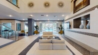 Located at 5290 Big Island Drive in Jacksonville, Florida, this single-story community clubhouse presents a well-appointed gathering space designed with a contemporary aesthetic. The grand lobby serves as the centerpiece, featuring soaring double-height ceilings, large-format tile flooring, and floor-to-ceiling glass doors that frame views of the outdoor pool area beyond. Decorative starburst wall sconces and recessed lighting illuminate the space, while a mosaic tile accent wall adds texture and visual interest alongside built-in display niches with mounted flat-screen televisions.

The lounge area within the lobby is furnished with neutral, modular seating arrangements anchored by area rugs, creating an inviting space for socializing. Adjacent to the main lobby, a bar area features a lengthy granite-topped counter with bar seating, warm wood cabinetry, pendant lighting, and a beverage station with a sink. A separate casual lounge space showcases blue-toned walls, wood-look flooring, bold abstract artwork, and comfortable sectional seating.

The game room is equipped with a pool table and shuffleboard, complemented by textured accent walls and vibrant artwork. A private meeting nook with a round wood table and modern chairs benefits from generous natural light through large windows overlooking a landscaped courtyard.