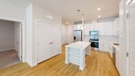 Located at 35205 Tupelo Cir in Frankford, DE, this well-appointed 2-bedroom, 2-bathroom single-floor home offers a clean, modern aesthetic throughout. The open-concept kitchen and living area serves as the heart of the home, featuring crisp white shaker cabinetry, white quartz countertops, a central island with built-in shelving, stainless steel appliances including a refrigerator with ice maker, range, microwave, and dishwasher, all complemented by stylish pendant lighting and recessed fixtures. Light wood-tone flooring flows throughout the main living areas, enhancing the bright, airy feel. The bedrooms are carpeted for comfort, each equipped with a ceiling fan and windows with blinds that invite natural light and outdoor views. The primary bedroom is a generous size and includes a walk-in closet with wire shelving organization. The primary bathroom features a wide white vanity with quartz countertop, a large mirror, and direct access to the walk-in closet. Additional highlights include four closets for ample storage, a dedicated laundry area, and a utility room. The home's neutral color palette and modern finishes create a cohesive, move-in-ready living environment.