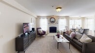 This single-floor residence offers a thoughtfully designed layout that balances comfort and functionality across its key living spaces. The kitchen is well-equipped with rich dark wood cabinetry, granite countertops, and a full suite of stainless steel appliances, including a side-by-side refrigerator with ice and water dispenser, an electric range with overhead microwave, and a deep sink. Light tile flooring and a patterned area rug add warmth to the space. The living room serves as the centerpiece of the home, anchored by a classic white-framed fireplace flanked by large windows dressed in sheer curtains that invite natural light. Plush carpeting, a ceiling light fixture, and an open layout create a welcoming atmosphere. Adjacent to the living room, the dining area features a round glass-top table set beneath a ceiling light, with two-tone wall paint and framed abstract artwork providing a polished aesthetic. The bathroom is finished with matching dark wood cabinetry, granite countertops, a large vanity mirror with a multi-bulb light bar, and a shower-tub combination. Throughout the space, neutral tones, consistent cabinetry finishes, and carpeted living areas create a cohesive and comfortable environment.