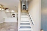 Located at 1214 Bradley Bowen Drive in Valdosta, GA, this two-story home offers a well-organized layout spread across two floors. The main level features an open-concept living, dining, and kitchen area bathed in natural light from plantation-shuttered windows. The kitchen is outfitted with white shaker-style cabinetry, gleaming white countertops, a peninsula sink, and a full suite of stainless steel appliances including a refrigerator, range, and microwave. Wood-look plank flooring runs throughout, lending a clean, cohesive aesthetic to the space. A staircase with white risers, gray treads, and a sleek metal handrail connects the two floors, with a pantry conveniently positioned at the top landing. The main level also includes a laundry area, utility spaces, a patio, and a bathroom. Upstairs, two bedrooms each feature ceiling fans, closets, and continued wood-look flooring. The primary bedroom is generously proportioned with its own dedicated closet space. Two additional bathrooms on the upper level include tub-shower combinations and clean white vanities with brushed nickel fixtures. The home also includes an office and multiple hallways for easy circulation. Outside, a newly constructed cedar privacy fence encloses the backyard, offering a secure outdoor retreat.