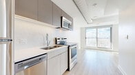 Located at 46 Flora St in Ottawa's vibrant Centretown neighbourhood, this modern studio unit offers a thoughtfully designed open-concept layout that efficiently combines the living, dining, and kitchen areas into one cohesive space. Light wood-tone vinyl flooring runs throughout, lending warmth and continuity to the interior.

The contemporary kitchen is well-appointed with stainless steel appliances — including a refrigerator, electric range, over-the-range microwave, and dishwasher — complemented by two-tone cabinetry in light wood and dark charcoal finishes, a double undermount sink, and a light quartz countertop. Exposed ductwork along the kitchen ceiling adds an industrial design accent.

The open living area is bright and airy, flooded with natural light through expansive floor-to-ceiling windows and a sliding glass door that opens to a balcony, offering sweeping views of the Ottawa skyline. Two closets provide practical storage solutions within the unit.

A full bathroom and in-unit laundry complete the layout, ensuring everyday convenience. The clean white walls, recessed lighting, and minimalist finishes throughout give the space a crisp, modern ambiance well-suited for urban living in one of Ottawa's most walkable and dynamic neighbourhoods.