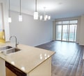 This 610-square-foot, single-floor one-bedroom unit at 885-905 Southdale Road in London, Ontario offers a practical and well-appointed layout. The combined kitchen and living area forms the heart of the unit, with wood-look laminate flooring extending throughout. The kitchen features white cabinetry, light stone countertops with a decorative tile backsplash, stainless steel appliances including a fridge, stove, and built-in microwave, and a peninsula with an integrated double sink and pendant lighting overhead, providing additional seating and prep space.

The living area is bright and open, with sliding glass doors leading to a balcony that offers expansive city views. The bedroom measures 160 square feet, includes a double closet, and is served by a large window with similarly elevated outdoor views, allowing for abundant natural light. Neutral-toned walls and clean white baseboards maintain a consistent, modern aesthetic throughout.

A dedicated laundry room houses a stacked washer and dryer unit on tile flooring, adding a functional convenience seldom found in units of this size. The overall design is clean and contemporary, with a neutral palette that offers versatility for a range of interior styles.
