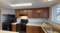 This single-floor, 2-bedroom, 2-bathroom residence offers a practical and comfortable layout designed to maximize everyday livability. The kitchen features warm honey-toned cabinetry with ample upper and lower storage, light granite-style countertops, a black appliance suite including an electric range and refrigerator, and a built-in range hood — all beneath a textured ceiling with overhead lighting. Both bathrooms are finished consistently, each offering a single-sink vanity with wood cabinetry, a tub/shower combo, wall-mounted storage cabinet, and clean white fixtures throughout. The living area is generously sized, carpeted in a neutral brown tone, and includes a ceiling fan with light kit, creating a comfortable and airy atmosphere. Natural light filters in through windows with views to the exterior. Both bedrooms are well-proportioned, carpeted, and equipped with ceiling fans. The primary bedroom is notably spacious, featuring multiple closet doors that provide abundant storage options, along with a private en-suite bathroom. The second bedroom mirrors the warm, neutral palette and benefits from natural light through a window. The overall design is cohesive, practical, and move-in ready.