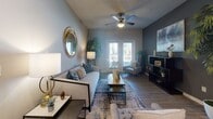 Located at 9102 FM 2920 in Tomball, Texas, this single-story residence offers a well-appointed layout with a cohesive contemporary design throughout. The living room serves as a central gathering space, anchored by wood-look flooring, a ceiling fan, and a bold dark accent wall that creates a striking focal point. French doors invite natural light and provide access to an outdoor area, enhancing the open, airy feel of the room. The kitchen features dark espresso cabinetry, granite-style countertops, black appliances, and light wood-look flooring, combining functionality with a sleek, modern aesthetic. Adjacent to the kitchen, the dining area accommodates a round dark-wood table surrounded by upholstered chairs, complemented by decorative wall art and mirrors. The bedrooms are comfortably appointed with plush carpeting, generous natural light from large windows, and ample space for furnishings. Each bathroom is finished with dark vanity cabinetry, granite-style countertops, wood-look tile flooring, and a tub-shower combination with tile surround. Throughout the space, neutral wall tones, curated décor, and consistent finishes create a harmonious and inviting atmosphere suited for everyday living.