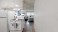 Located on Vanowen Street in Van Nuys, Los Angeles, this efficiently designed single-floor unit offers a bright and functional layout that maximizes every square foot. The open-concept living area is finished with light wood-look flooring throughout, creating a clean and cohesive aesthetic. White walls and a textured ceiling enhance the sense of openness, while a wall-mounted AC unit ensures year-round comfort. A large window floods the space with natural light and offers a pleasant view of surrounding greenery, adding a touch of the outdoors to the interior. The living area comfortably accommodates a full seating arrangement, making it a welcoming and practical space for everyday living. The kitchenette is equipped with a white gas range, overhead ventilation hood, and white cabinetry, providing essential cooking amenities in a compact footprint. A breakfast bar with seating connects the kitchen to the living area, adding both functionality and a social element to the layout. The bathroom features a full-sized soaking tub and shower combination, elegantly framed by marble-style surround walls in warm beige tones, offering a clean and polished finish. This unit delivers a practical and well-appointed living experience in a convenient Los Angeles location.