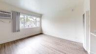 Located at 8561 De Soto Ave in the Canoga Park neighborhood of Los Angeles, this efficiently designed unit offers a clean, modern aesthetic across a single floor. The layout comprises a living room, kitchen, and bathroom, making smart use of every square foot.

The living room is the largest area of the unit, finished with light-toned laminate wood flooring that runs throughout. Crisp white walls and a large sliding window allow natural light to fill the space, with views of the surrounding neighborhood and palm trees visible outside. A wall-mounted smoke detector and clean baseboard trim reflect attention to detail throughout.

The galley-style kitchen is accessed from the living area and features white cabinetry, a stainless steel sink, a gas range, a ventilation hood, and a full-size refrigerator. Light beige ceramic tile flooring and white walls keep the space bright and practical. A pass-through counter connects the kitchen to the living area, enhancing the open feel.

The bathroom continues the clean, neutral palette with beige tile flooring, white walls, and a full bathtub and shower combo with chrome fixtures. The space is well-maintained and functional.

Overall, this unit presents a minimalist, move-in ready environment with consistent finishes throughout, suited for those seeking a practical and well-lit space in the Los Angeles area.