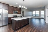 Located at 1709 Cresthill Ave in Royal Oak, Michigan, this single-floor residence offers a cohesive modern design defined by rich dark hardwood flooring, neutral gray walls, and clean white trim throughout. The open-concept kitchen serves as the centerpiece of the living space, showcasing dark espresso cabinetry that extends to the ceiling, light quartz countertops, and a uniquely shaped center island with an integrated sink and pendant lighting overhead. Stainless steel appliances—including a French door refrigerator, electric range, and built-in microwave—complement the kitchen's contemporary aesthetic. A dedicated pantry with adjustable shelving provides generous storage directly adjacent to the kitchen. The living area flows seamlessly from the kitchen, offering an open, airy feel with recessed lighting. Bedrooms are well-proportioned, benefiting from natural light through large windows. The bathroom features dark cabinetry paired with quartz countertops, an undermount sink, brushed nickel fixtures, and a framed mirror. Walk-in closets equipped with adjustable shelving and hanging rods provide organized, practical storage. The overall design maintains a consistent, polished finish throughout every room.