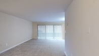 This single-floor residence offers a thoughtfully designed layout across a comfortable footprint, comprising one bedroom, two bathrooms, a living room, kitchen, and a dedicated closet. The living room is the heart of the home, featuring neutral-toned carpet, clean white baseboards, and a large sliding glass door dressed in vertical blinds that floods the room with abundant natural light and provides access to the outdoors. The kitchen is well-equipped with warm wood cabinetry, granite-style countertops, and a full suite of black appliances including a gas range, built-in microwave, and dishwasher, all set on light tile flooring. The spacious primary bedroom continues the neutral carpet theme and is brightened by a large window with horizontal blinds, creating a calm, restful atmosphere. It is complemented by a walk-in closet outfitted with dual hanging rods and shelving for ample storage. Both bathrooms are finished with tile flooring, and one features a white vanity with a mirrored medicine cabinet and globe lighting. Throughout the residence, a consistent warm beige palette and clean finishes create a cohesive, move-in-ready ambiance.