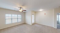 This single-floor unit is designed with a practical, open layout that connects its key living spaces efficiently. The living area is generously sized, featuring neutral-toned carpet, a ceiling fan with integrated lighting, and access to an exterior door that allows natural light to flow in through its window panel. A secondary carpeted room off the main living space offers additional flexibility for use as a bedroom or sitting area.

The kitchen is a functional highlight, equipped with dark espresso-toned cabinetry, granite-style countertops, and a full suite of black appliances including a refrigerator, electric range, built-in microwave, and a double-basin stainless steel sink. Wood-look flooring grounds the kitchen's rich, contrasting aesthetic.

The bedrooms are carpeted and finished in warm neutral tones, each with windows fitted with blinds for light control and privacy. Paneled white doors provide clean transitions between spaces.

Two bathrooms serve the unit: one features a granite-topped vanity with dark cabinetry and a shower-tub combo, while the second offers a walk-in shower stall with chrome fixtures and grab bars, set atop light tile flooring. Throughout, the unit maintains a consistent, understated palette.