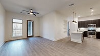 This well-designed single-floor unit offers two bedrooms and two bathrooms within a thoughtfully organized layout. The open-concept living and kitchen area serves as the central hub of the space, featuring light wood-style flooring, crisp white walls, and a ceiling fan overhead. A windowed door allows natural light to filter into the living room, while built-in shelving adds a functional architectural detail to one wall.

The kitchen is a standout feature, equipped with dark wood-grain cabinetry, stainless steel appliances, a subway tile backsplash, and a large island with light quartz countertops and a matte black faucet. A decorative wine rack built into the upper cabinetry adds a refined touch.

The primary bedroom is generously sized, featuring large windows with outdoor views, a ceiling fan, and access to a private en-suite bathroom. The bathroom includes a glass-enclosed shower, a dark vanity with a single sink, and wood-style flooring consistent with the rest of the unit.

The secondary bedroom offers similar flooring and gray-toned doors. A dedicated laundry room houses a full-size washer and dryer, while a spacious walk-in closet with multi-level wire shelving provides ample storage.