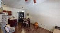 This single-floor residence offers a thoughtfully designed layout that balances comfort and functionality across its key living spaces. The dining area is a welcoming focal point, showcasing rich hardwood-style flooring, vaulted ceilings with a ceiling fan, and a pendant light that illuminates a dark-wood dining table set for four. A striking dark cabinet hutch provides display and storage, adding a classic touch to the space, which connects seamlessly to the adjacent kitchen. The kitchen is equipped with deep cherry-toned cabinetry, a gas range, dishwasher, refrigerator, and light stone countertops, all set atop easy-care tile flooring. The bedroom features plush carpeting, ceiling fan, and a standout set of French doors that open to a private outdoor balcony, flooding the room with natural light and offering an outdoor retreat. The full bathroom includes a tub-shower combination, a rich wood vanity with a single sink, tile flooring, and wall-mounted lighting for a clean, functional finish. A dedicated in-unit laundry closet with a stacked washer and dryer adds everyday convenience. Throughout the residence, neutral wall tones and consistent design choices create a cohesive and inviting atmosphere.