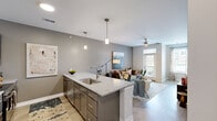 This single-floor residence at The Carlyle at Chatham Hills offers a thoughtfully designed open-concept layout that efficiently utilizes its space. The kitchen serves as a central feature, showcasing dark gray shaker-style cabinetry, stainless steel appliances, a white subway tile backsplash, and a granite-topped island with an undermount sink and seating for two. Pendant lighting above the island adds a modern accent. The kitchen flows seamlessly into the living room, which features light wood-style flooring, neutral gray walls, a ceiling fan, and a glass door with adjacent windows that invite natural light and provide outdoor views.

The primary bedroom features soft carpeting, a teal accent wall, a ceiling fan, and a window overlooking the surrounding community. The second bedroom mirrors similar finishes and natural light access. Both bathrooms are well-appointed, with one featuring a walk-in shower lined with white subway tile, brushed nickel fixtures, and dark cabinetry with granite countertops.

A light-toned hallway with wood-style flooring connects the bedrooms and bathrooms, contributing to the clean, cohesive aesthetic found throughout this contemporary Westfield residence.