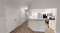 This two-story residence at Cooper Creek offers a well-organized layout designed for comfortable everyday living. The main level centers around an open kitchen and living area, where wood-style flooring runs throughout, creating a cohesive and clean aesthetic. The kitchen is outfitted with white shaker-style cabinetry, light stone countertops, a stainless steel sink, dishwasher, refrigerator, and range with microwave above. A curved peninsula provides additional prep space and naturally defines the transition between the kitchen and the adjoining living area. A sliding glass door leads directly to a private outdoor green space, allowing natural light to fill the room. The entry level also includes closet storage and utility access. Upstairs, the bedrooms are finished with plush carpeting and ceiling fans, lending a quieter, more restful atmosphere. Several bedrooms feature windows with views of surrounding greenery, and at least one includes a dedicated closet with bifold doors and built-in hanging rods. The upper level also connects back to the staircase, which is visible in the open layout. Throughout, neutral wall tones and consistent finishes give the home a clean, move-in-ready appearance.