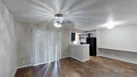 Located in the sought-after 78704 corridor of Austin, Texas, this single-story residence at 1304 Summer Oak Drive offers a practical and functional layout with a comfortable, lived-in character. The open-concept living and kitchen area serves as the heart of the home, where rich, dark hardwood-style flooring runs throughout, grounding the space with warmth and visual continuity. A ceiling fan centered above the living area provides both comfort and light, while vertical blinds along the sliding glass door allow for adjustable natural light and outdoor access. The kitchen is defined by a peninsula-style breakfast bar that creates a natural division between the cooking and living zones without sacrificing the open feel. Dark cabinetry lines the kitchen walls, complemented by black appliances including a full-size refrigerator and a range, creating a cohesive, modern aesthetic. A textured ceiling adds character overhead throughout the main living area. The neutral wall tones throughout provide a versatile backdrop, making the space easy to personalize. This home's single-floor layout ensures seamless flow and accessibility across all areas, making it a straightforward and well-connected living environment in a desirable Austin location.