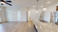 Located at 2411 Wave Rock Way in Knoxville, Tennessee, this single-story, one-bedroom, one-bathroom residence offers a well-designed layout with modern finishes throughout. The heart of the home is an open-concept kitchen and living area, where rich dark wood cabinetry pairs elegantly with granite countertops on a substantial center island equipped with a dual-basin sink. Stainless steel appliances, including a refrigerator, range, microwave, and dishwasher, complete the kitchen. Pendant lighting above the island and recessed ceiling lights illuminate the space, while light hardwood-style flooring extends throughout the main living area, adding warmth and continuity. The living area benefits from natural light through a large window and is complemented by a ceiling fan for year-round comfort. The bedroom features plush carpeting, a generously sized window with views of the surrounding neighborhood, and ample wall space. The bathroom is finished with a full tub-shower combination and clean, neutral tile flooring. A dedicated laundry area with utility connections adds everyday convenience. The overall aesthetic is clean, bright, and functional, making this a practical and comfortable residence in the Knoxville area.