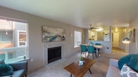 Located at 12188 Cloudy Peak Lane NW in Silverdale, Washington, this single-floor residence offers a well-organized layout designed for comfortable everyday living. The open-concept living and dining area serves as the heart of the home, centered around a tile-surround fireplace that adds warmth and character. Soft carpeting runs throughout the living spaces, and large windows on multiple walls flood the room with natural light while framing views of the surrounding trees. A glass door leads to an outdoor balcony, extending the living space outdoors. The kitchen is equipped with stainless steel appliances including a range and refrigerator, complemented by two-tone cabinetry — white uppers and gray lowers — stone-look countertops, and wood-look flooring. It connects seamlessly to the dining area, making it ideal for entertaining. The primary bedroom is generously sized with plush carpet and a window for natural light. A second bedroom provides flexibility as a guest room or home office, also featuring carpet and a bright window. The full bathroom includes a vanity with updated cabinetry and a tub-shower combination. A dedicated laundry room with a full-size washer and dryer adds everyday convenience to this thoughtfully designed home.