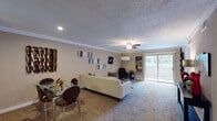 This single-floor residence offers a thoughtfully arranged layout that balances comfort and functionality across multiple living areas. The open-concept living and dining space serves as the heart of the home, featuring wall-to-wall carpet, crown molding, and a textured ceiling with a ceiling fan overhead. Recessed lighting complements the natural light streaming through a sliding glass door that opens to an outdoor area, enhancing the room's bright and welcoming ambiance. A glass-top dining table sits comfortably alongside the living area, creating a seamless flow between the two spaces.

The galley-style kitchen is efficiently designed with dark espresso cabinetry, dark granite countertops, and a mosaic tile backsplash. Stainless steel appliances, including a refrigerator, electric range, dishwasher, and built-in microwave, line both sides of the kitchen, while tile flooring adds a clean, practical finish.

The primary bedroom is generously proportioned, featuring plush carpet, crown molding, ceiling fan, and multiple windows that bring in ample natural light. A dark-toned open shelving unit serves as a stylish room divider. An additional room functions well as a home office or guest space, also carpeted and naturally lit. The bathroom features full stone-look tile walls, a soaking tub with glass enclosure, and coordinating tile flooring.