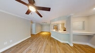 This well-appointed single-floor residence offers a thoughtfully designed open-concept layout that seamlessly connects the living, dining, and kitchen areas. Warm wood-look flooring flows consistently throughout the space, complemented by neutral-toned walls and crisp white trim that create a clean, cohesive aesthetic.

The kitchen is a standout feature, showcasing white shaker-style cabinetry, light quartz countertops, a classic subway tile backsplash, and a full suite of stainless steel appliances including a range, microwave, and dishwasher. A curved peninsula with an integrated sink extends into the living area, providing both additional prep space and a natural division between rooms.

The living area is generously proportioned, featuring crown molding, ceiling fans, and track lighting. Multiple sliding glass doors open to the outdoors, flooding the interior with natural light and offering pleasant views of mature greenery and landscaping.

The bedrooms are spacious and well-lit, with one featuring an arched window that adds architectural character. Additional rooms include a walk-in closet area and a dedicated laundry space. Throughout the home, ceiling fans provide comfort, and recessed lighting adds a polished finishing touch. The overall ambiance is bright, airy, and move-in ready.