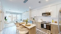 This well-appointed one-bedroom residence at 925 S Glebe Rd offers a thoughtfully designed open-concept layout that maximizes every inch of its comfortable footprint. Light wood-tone flooring flows throughout, unifying the space with a warm, contemporary aesthetic.

The kitchen is a standout feature, showcasing a two-tone design with crisp white upper cabinetry and natural wood-finish lower cabinets. Stainless steel appliances — including a refrigerator, range, and built-in microwave — anchor the space, while a central island with a white quartz countertop and seating for two serves as an ideal casual dining and gathering area. A linear pendant light adds a modern finishing touch overhead.

The open living area benefits from generous windows that invite abundant natural light and offer views of the surrounding streetscape. The neutral color palette and clean lines create a calm, inviting atmosphere throughout.

The primary bedroom is a well-sized retreat, featuring a large window with outdoor views, light-toned walls, and elegant ceiling lighting with a sculptural gold fixture. A dedicated closet provides convenient storage.

The bathroom is finished with light tile flooring, a full soaking tub with shower, and a wood-toned vanity with a white countertop, maintaining the residence's cohesive modern design language throughout.