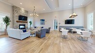 Located at 85 Washington St in Plainville, MA, this well-appointed single-story community space spans a generous footprint designed for both comfort and functionality. The welcoming entrance lobby features polished marble tile flooring, a coffered ceiling with an elegant chandelier, and decorative planters that set a refined tone throughout.

The expansive kitchen and living area serves as the heart of the space. The kitchen is outfitted with rich dark cabinetry, light stone countertops, stainless steel appliances, and warm wood-look flooring. Stylish pendant lighting illuminates a central dining table, making it ideal for gatherings. The adjoining living room boasts soaring ceilings, a striking stacked-stone fireplace, a statement chandelier, and large windows that bathe the room in natural light and offer views of the surrounding neighborhood.

The office area includes two dedicated conference rooms. One features an accent stone wall, a large flat-screen display, and executive seating for productive meetings. The other is lined with a row of oversized windows providing abundant daylight and outdoor views, creating a bright and professional environment. Throughout, consistent wood-look flooring, crown molding, and a neutral color palette contribute to a cohesive and polished ambiance.