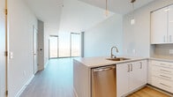 Located at 401 S. Graham Street in Charlotte, NC, this one-bedroom, one-bathroom unit offers a thoughtfully designed layout with modern finishes throughout. Light wood-tone flooring flows continuously across the open living and kitchen areas, complementing the neutral palette of the crisp white walls and high ceilings that enhance the sense of space.

The living area is anchored by dramatic floor-to-ceiling windows that frame expansive panoramic views of the Charlotte skyline and surrounding neighborhoods, flooding the space with abundant natural light. The kitchen features a peninsula with an undermount sink and gold-tone faucet, white flat-front cabinetry, a subway tile backsplash, and a full suite of stainless steel appliances including a refrigerator, range, and built-in microwave.

The bedroom benefits from the same impressive floor-to-ceiling glazing, offering sweeping elevated views, and connects to a well-appointed walk-in closet with wire shelving systems on multiple walls. The bathroom includes a long white vanity with ample storage, a framed mirror, and a glass-enclosed tub and shower combination finished with classic white subway tile. A clean entryway with multiple interior doors completes this well-organized, light-filled residence.