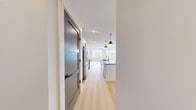 This thoughtfully designed one-bedroom, one-bathroom residence in Billerica, MA offers a clean, modern aesthetic with high-quality finishes throughout its well-proportioned single-floor layout. Light hardwood flooring runs continuously through all rooms, creating a cohesive and airy feel.

The open-concept kitchen and living area serves as the heart of the home. The kitchen is outfitted with sleek white cabinetry, dark gray quartz countertops, stainless steel appliances including a full-size refrigerator, range, and built-in microwave, and a central island with an undermount sink. Stylish pendant lighting adds a refined touch above the island.

The living area is bright and spacious, benefiting from multiple large windows that invite natural light and offer views of the surrounding neighborhood and greenery. A sliding glass door opens to a private balcony, further extending the living space outdoors.

The bedroom is generously sized with dual windows framing tree-lined views, providing a calm and private retreat. The bathroom features a tiled walk-in shower with white subway tile walls, a hexagonal mosaic tile floor, and a built-in niche. Charcoal-gray shaker-style interior doors with matte black hardware add a consistent, modern design element throughout the unit.